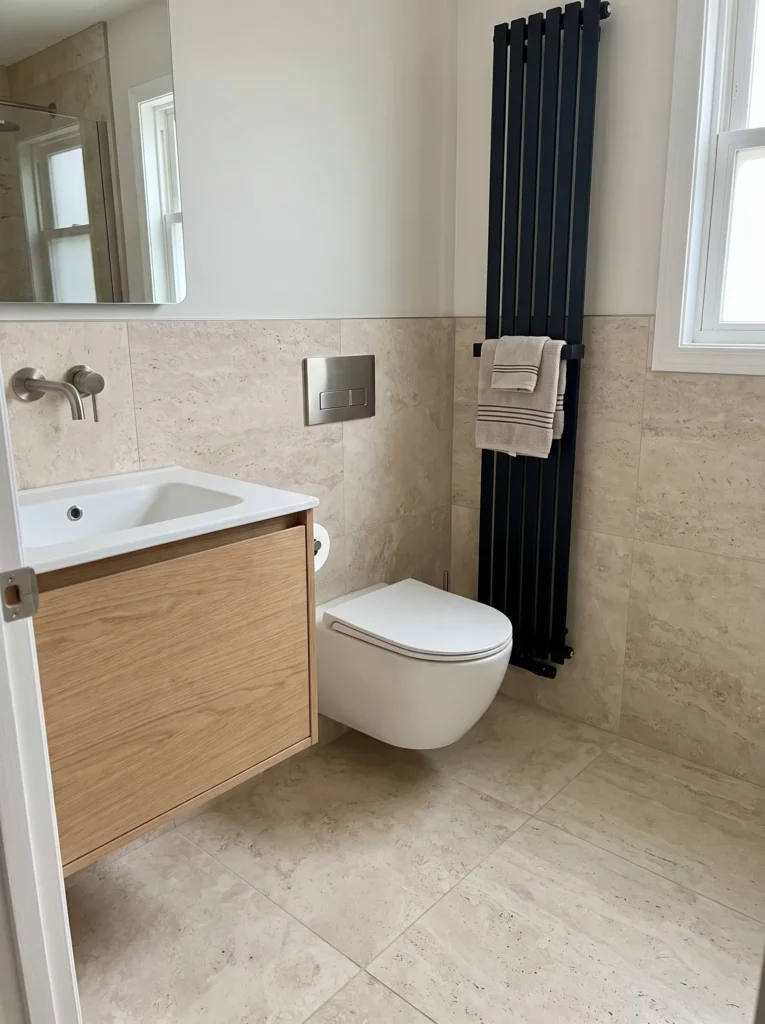 Small bathroom with a wall-hung toilet with concealed tank, a matching floating vanity, and a black vertical towel warmer radiator